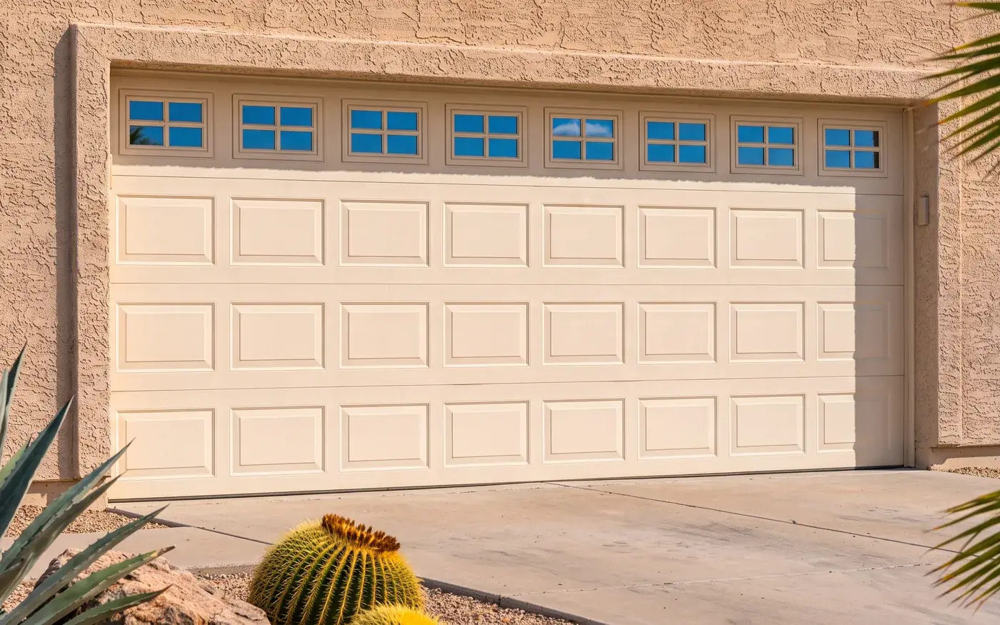 A closed cream raised-panel sectional garage door in a stucco surround, its top section glazed with small windows, seen straight on from the concrete driveway.
